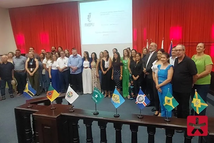 autoridades de pé, pousando para fotografias, a frente de um telão e cortinas vermelhas 