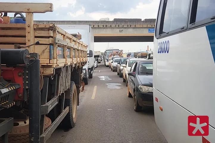 Imagem com veículos de pequeno e grande porte parados em fila na rodovia