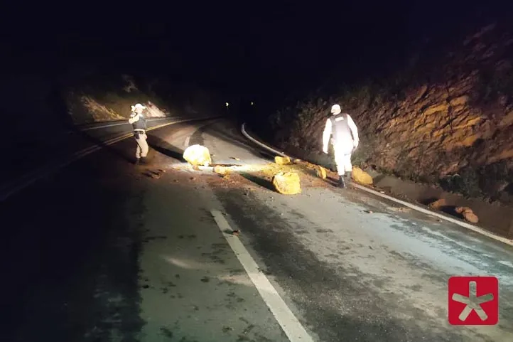 imagem colorida, periodo noturno e policiais retirando pedras da rodovia