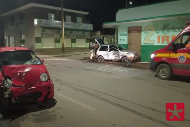 imagem colorida, com veículos nas cores vermelha e cinza, ambos danificados pela batida. No local uma viatura do Corpo de Bombeiros e policiais militares