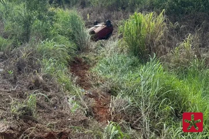 veículo tombado fora da pista em meio a vegetação, com as quatro rodas para cima.