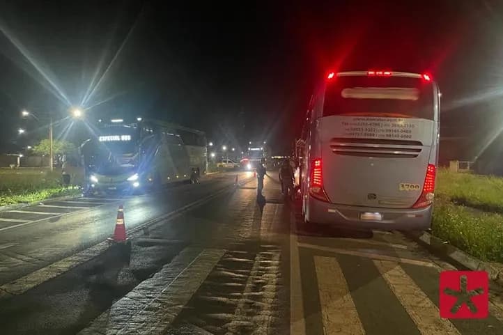 imagem colorida feita durante a noite, mostrando policiais ao lado de dois ônibus na rodovia