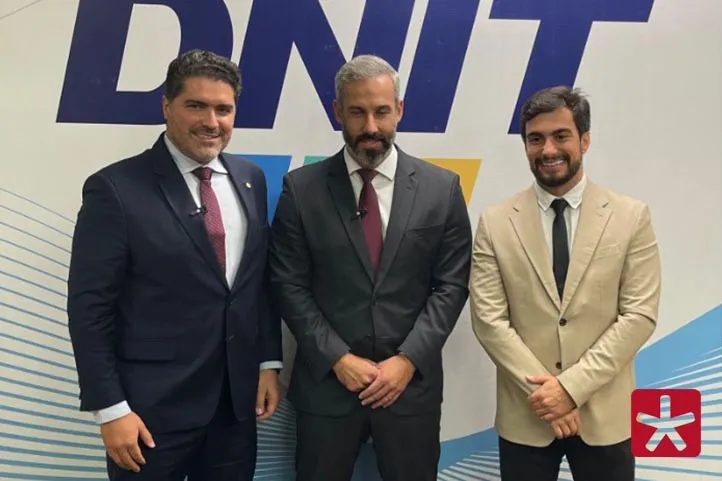 Imagem colorida, com o deputado Newton Cardoso Jr ao lado do diretor do DNIT Fabricio Oliveira e do vereador Vitor Porto. Atrás dos três uma parede com a inscrição DNIT