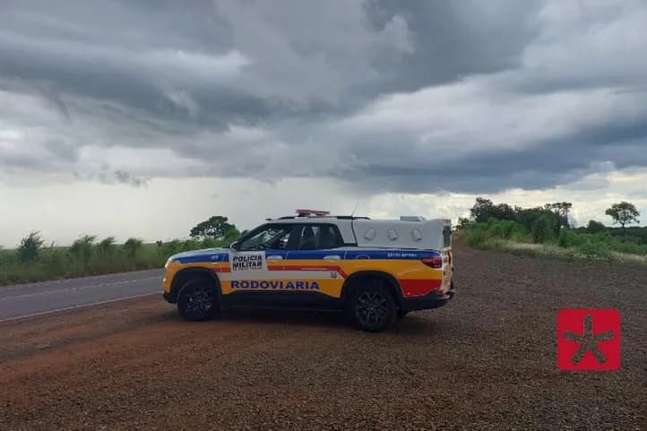 fotografia contendo viatura da Polícia Militar estacionada ao lado de rodovia com um fim de tarde ao fundo