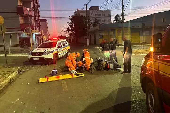 imagem colorida mostrando motocicleta caida no meio da rua com a vítima sendo atendida por militares do Corpo de Bombeiros próximo a viaturas da PM e Bombeiros