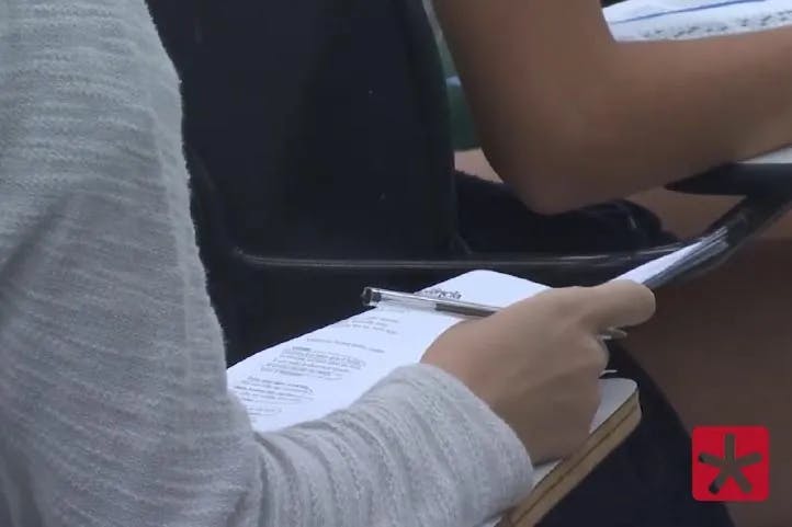 Imagem mostrando estudante em sala de aula com papel e caneta na mão durante prova